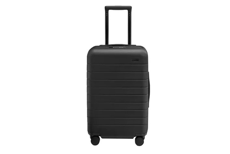 seven carry-on and checked bags lined up on a warehouse floor for comparison